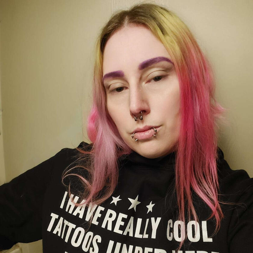 White person with pink and blonde hair, wearing a black hoodie.